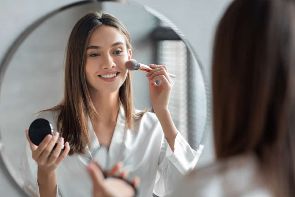 Attractive-Young-Woman-Doing-Daily-Makeup-While-Standing-Near-Mirror-In-Bathroom.jpeg